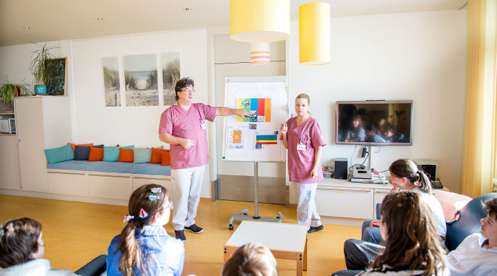 Kinder-Reha Schweiz, Wohngruppe, Pflegefachfrau und Pflegefachmann reden mit einer Gruppe von jungen Patient*innen