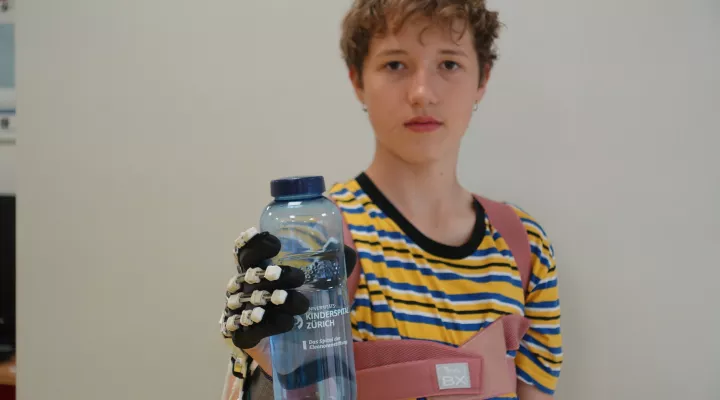 Junge hält mit PEXO Hand-Exoskelett eine Trinkflasche.