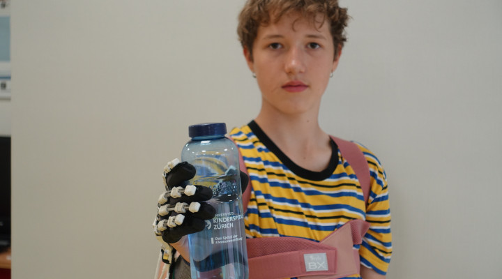 Junge hält mit PEXO Hand-Exoskelett eine Trinkflasche. 