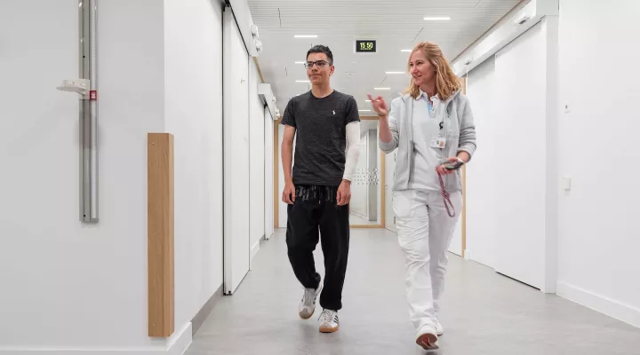 Patient Diego läuft mit Ärztin Sophie Böttcher durch Korridor.