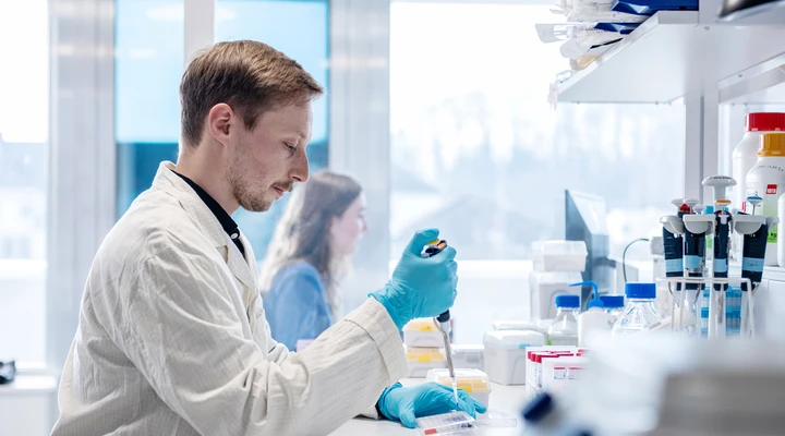 Ein Forscher im Laborkittel sitzt im Labor und arbeitet mit Pipette