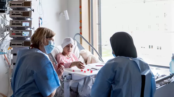 Eine junge Patientin liegt während Stammzelltransplantation im Spitalbett und spielt ein Würfelspiel
