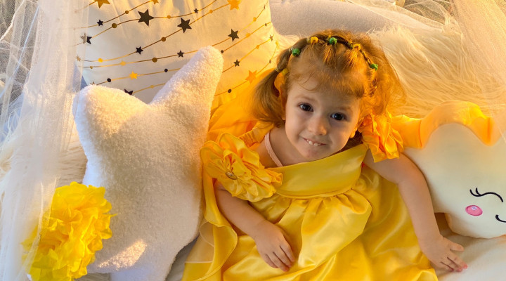 Kind mit spinaler Muskelatrophie in gelbem Kleid lächelt in die Kamera