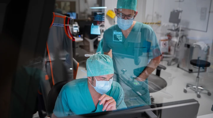 Zwei Ärzte in OP-Kleidung besprechen sich vor einem Computerbildschirm