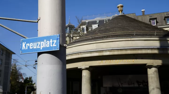 Ein Strassenschild mit der Aufschrift "Kreuzplatz" befestigt an einem Mast.