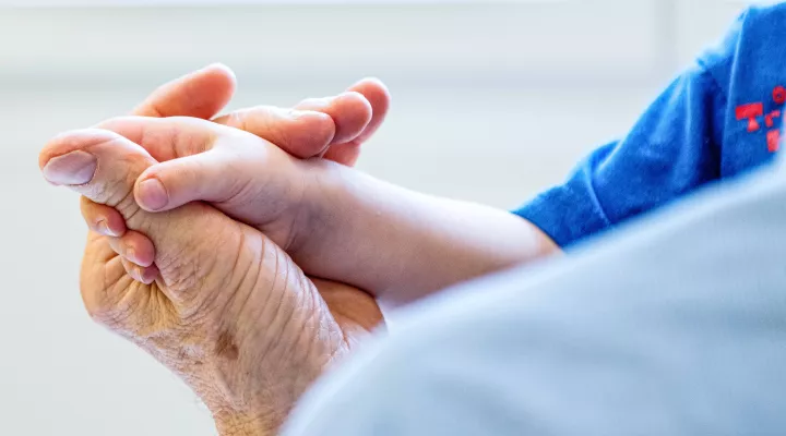 Eine Hand eines jungen Kindes liegt in der Hand einer älteren Person