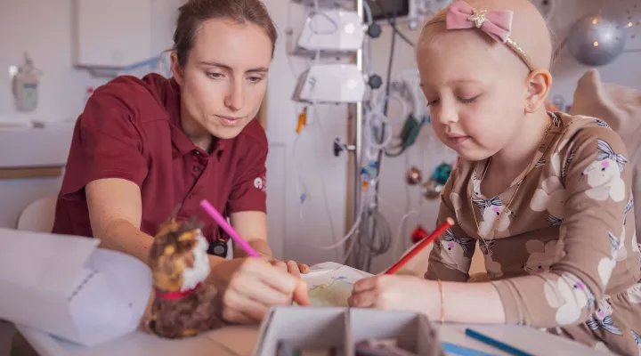 Eine junge Onkologie-Patientin malt ein Bild zusammen mit einer Spitallehrerin