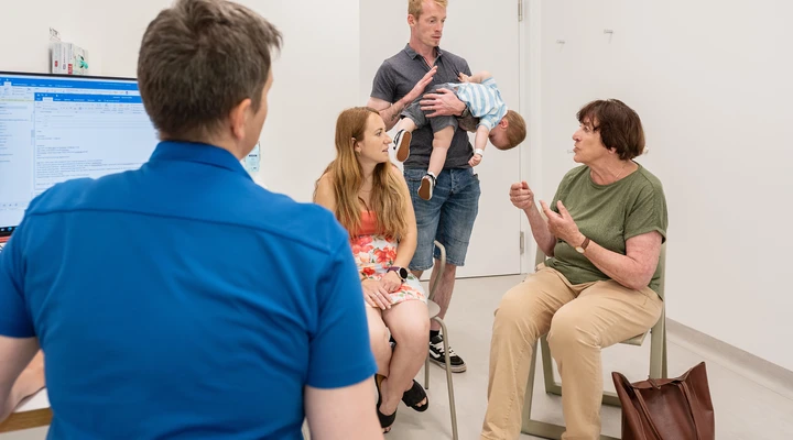 Eine Pflegefachfrau unterhält sich mit Patienteneltern im Untersuchungszimmer während eine Dolmetscherin für die Eltern übersetzt.