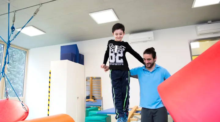 Physiotherapeut unterstützt Kind beim Balancieren