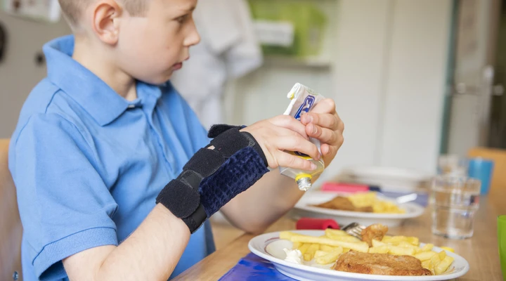Ein Junge mit einer Hand-Schiene isst Schnitzel-Pommes in der Kinder-Reha Schweiz
