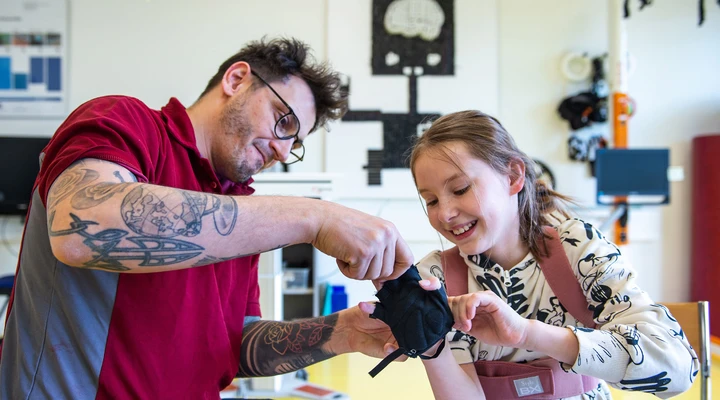 Ein Therapeut hilft einem jungen Mädchen in der Kinder-Reha Schweiz beim Anlegen eines Handschuhs
