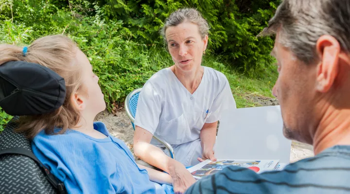 Eine Pflegeberaterin spricht mit einer Patientin im Rollstuhl und ihrem Vater