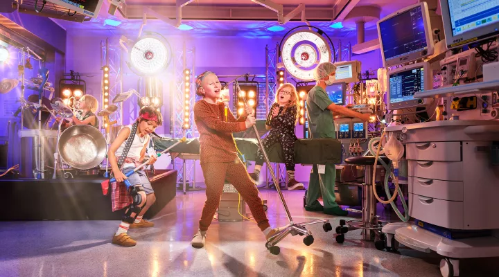 Vier Kinder rocken an Instrumenten im OP, daneben steht ein Arzt in grün.