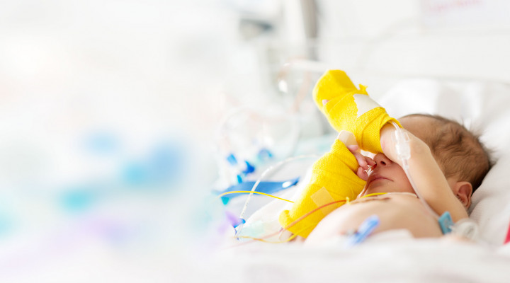 Neonatologie, Neugeborenes im Spitalbettchen mit gelben Verbänden an den Händen