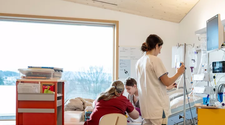 Pflegefachfrau hantiert am Infustionsständer am Bett eines Patienten