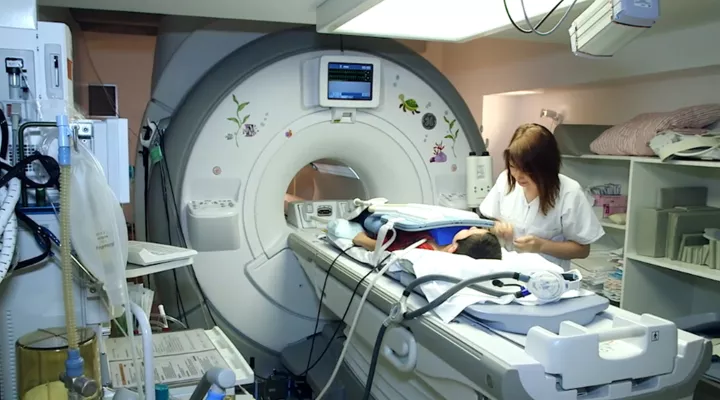 Ein Kind wird auf einer Trage in ein MRI gefahren, eine Fachperson steht daneben.