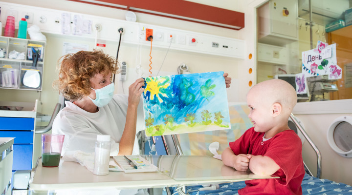 Ein krankes Kind malt ein Bild mit der Kunsttherapeutin Barbara Carnielli auf der Stammzelltransplantation- Station