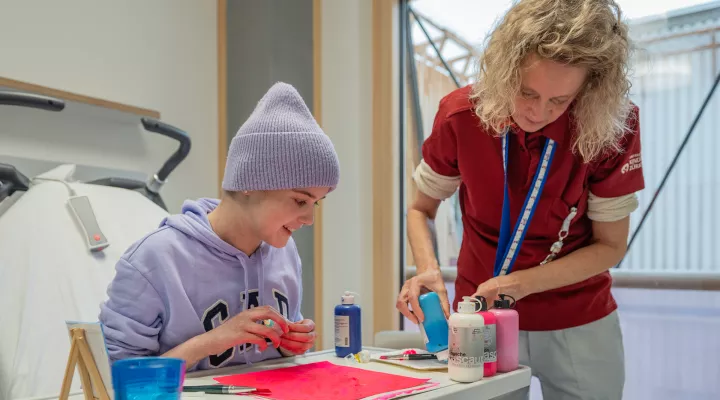 Eine Patientin beobachtet, wie eine Therapeutin Farbe auf ein Blatt gibt.