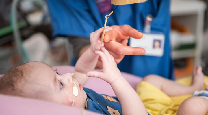Ein krankes Baby spielt mit einem Musikinstrument während einer Musiktherapie im Kinderspital Zürich