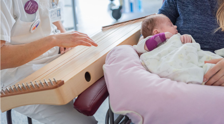 Die Musiktherapeutin spielt Monochord während eine Mutter das kranke Kind in den Armen hält