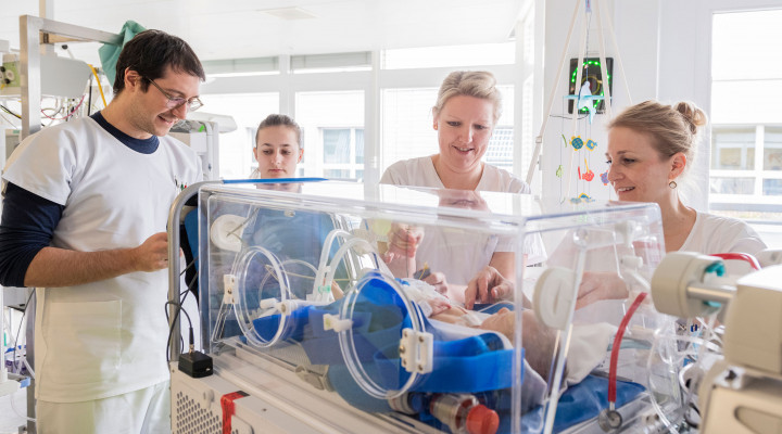 Das medizinische Team bespricht sich kurz vor der Untersuchung eines neugeborenes Baby in der Isolette