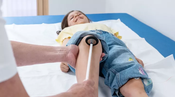 Neuropädiatrie, geschlossene Dysraphien, Reflexsuche am Bein eines Mädchens