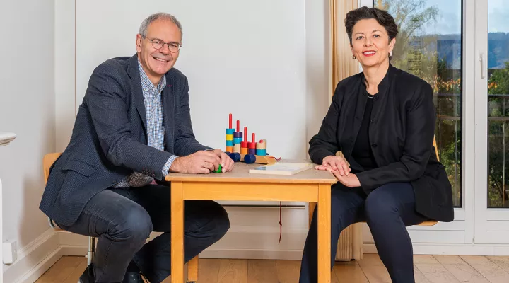 Oskar Jenni und Bea Latal sitzen an einem Kindertisch und lachen in die Kamera.