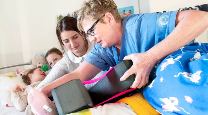 Kinder-Reha Schweiz, Pflegefachfrau zieht Kind Beinschiene an, Mutter hilft mit