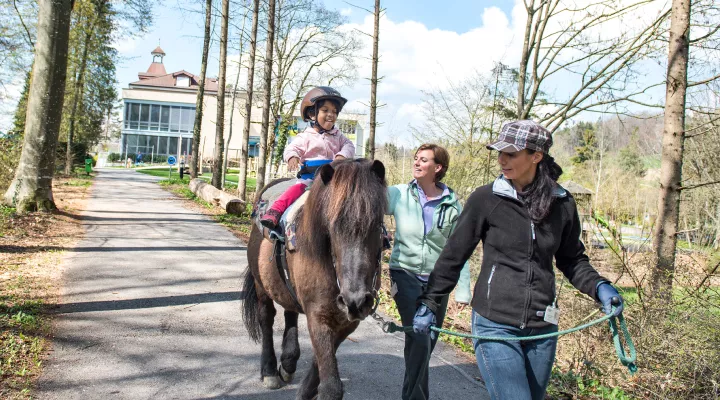 Kinder-Reha Schweiz, Hippotherapie, Therapeutinnen und Patientin beim Ausritt im Wald