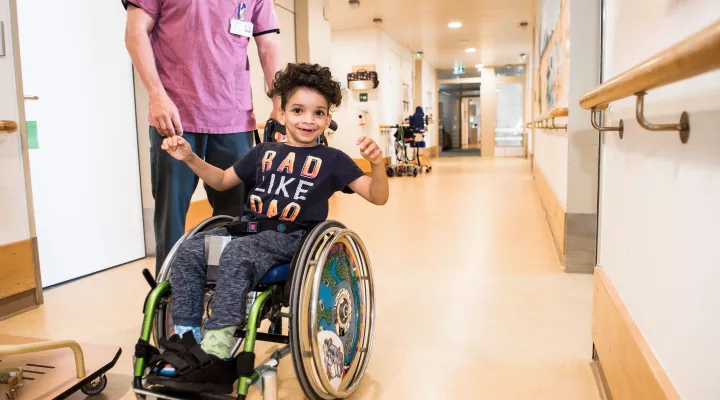 Kinder-Reha Schweiz, Patient im Rollstuhl mit Pflegefachmann im Gang