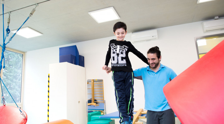 Kinder-Reha Schweiz, Physiotherapie, Patient balanciert auf Balken, Physiotherapeut stützt ihn