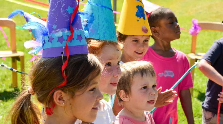 Fünf Kinder mit bunten, hohen Hüten auf dem Kopf stehen draussen.