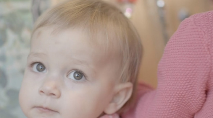 Ein kleines Kind mit blauen Augen und kurzen blonden Haaren schaut in die Kamera.