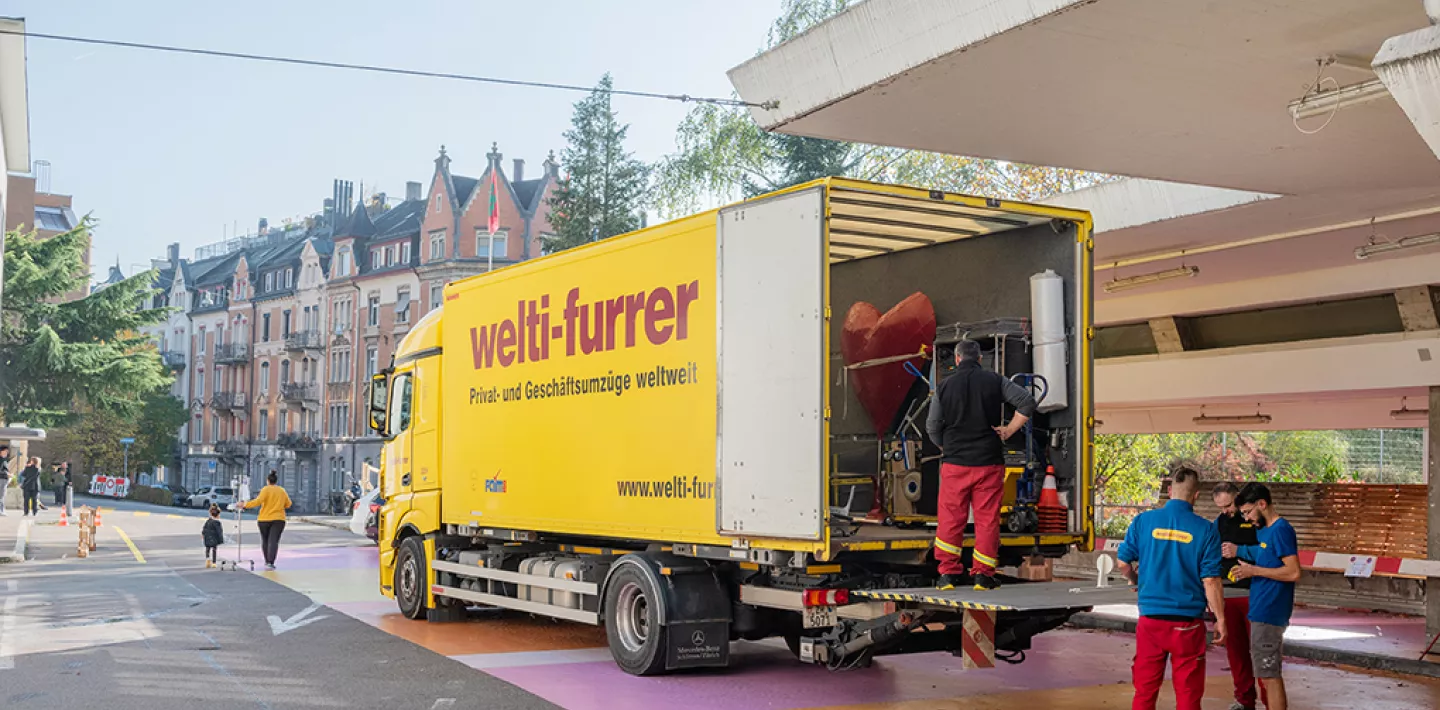 Drei Männer verladen Güter in einem gelben Lastwagen mit der Aufschrift "Welti-Furrer"