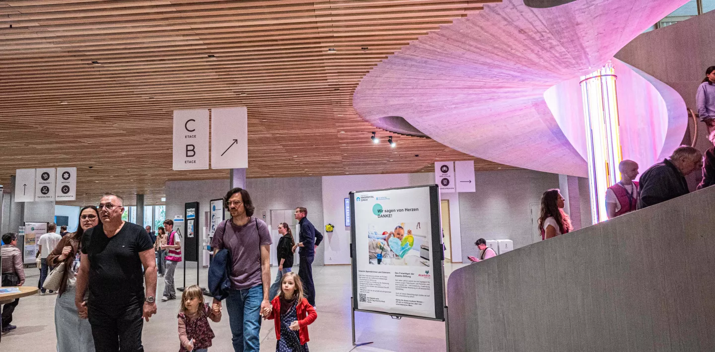 Besuchende im Hauptfoyer des Kinderspitals mit beleuchteter Rundtreppe