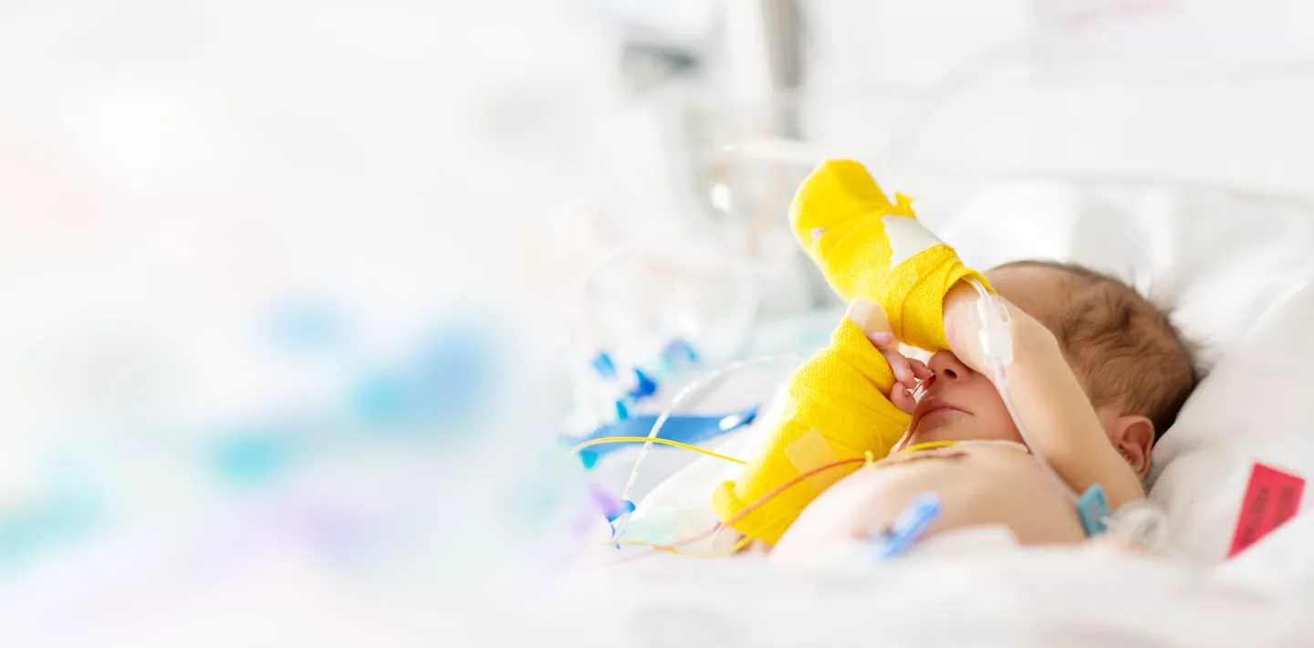 Neonatologie, Neugeborenes im Spitalbettchen mit gelben Verbänden an den Händen