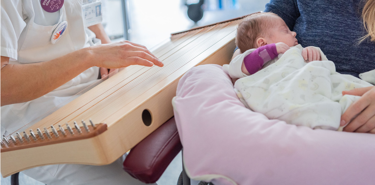 Die Musiktherapeutin spielt Monochord während eine Mutter das kranke Kind in den Armen hält