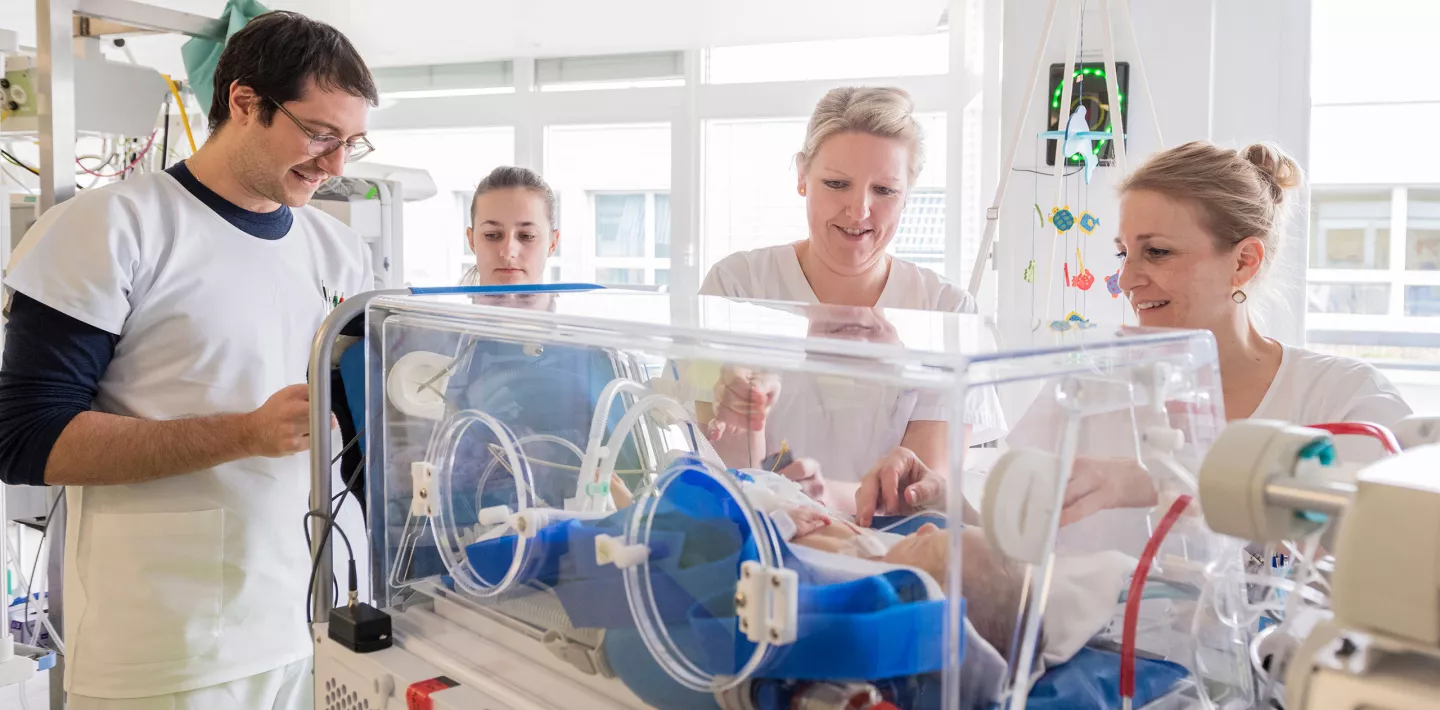 Das medizinische Team bespricht sich kurz vor der Untersuchung eines neugeborenes Baby in der Isolette