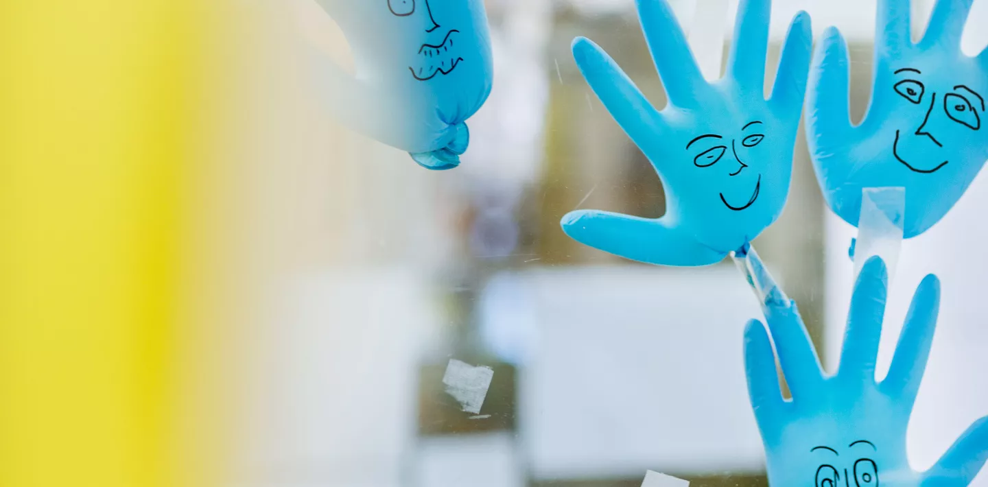 Blaue Plastikhandschuhe mit aufgemalten Gesichtern kleben an der Scheibe der Kabine, Stammzellentransplantation
