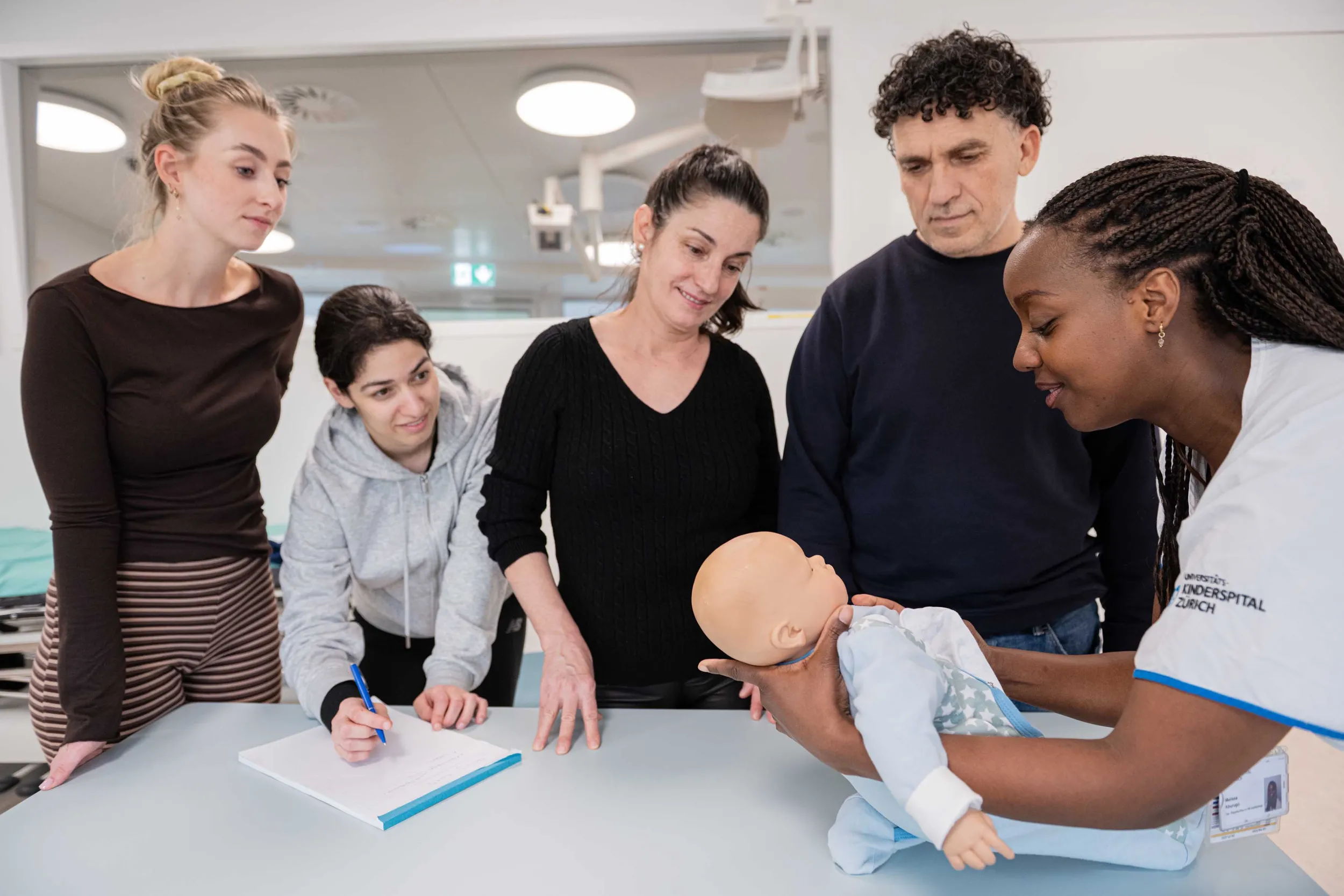 Auf einem Tisch liegt eine Baby-Puppe an der Erste-Hilfe Massnahmen gezeigt werden