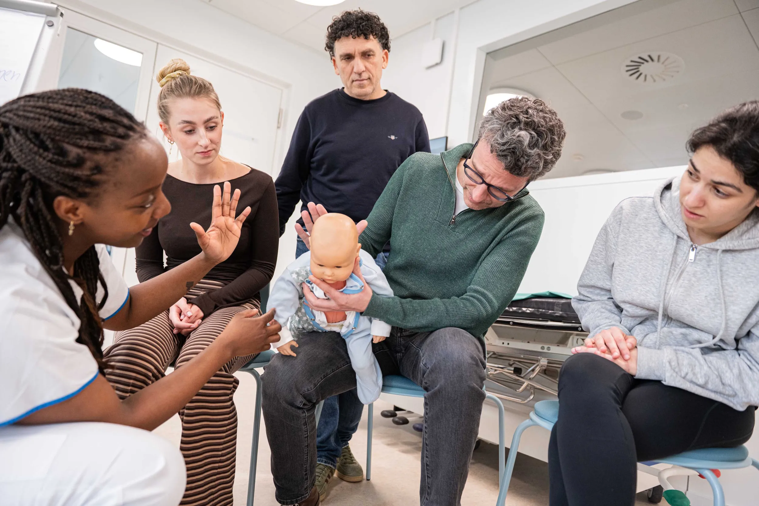 Eine Expertin Notfallpflege zeigt Eltern und Angehörigen Erste-Hilfe-Massnahmen an einer Babypuppe