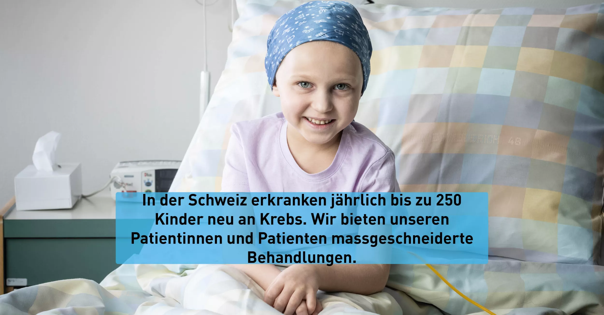 Eine Onkologiepatientin trägt ein Tuch um den Kopf. Sie sitzt in ihrem Bett und lächelt.