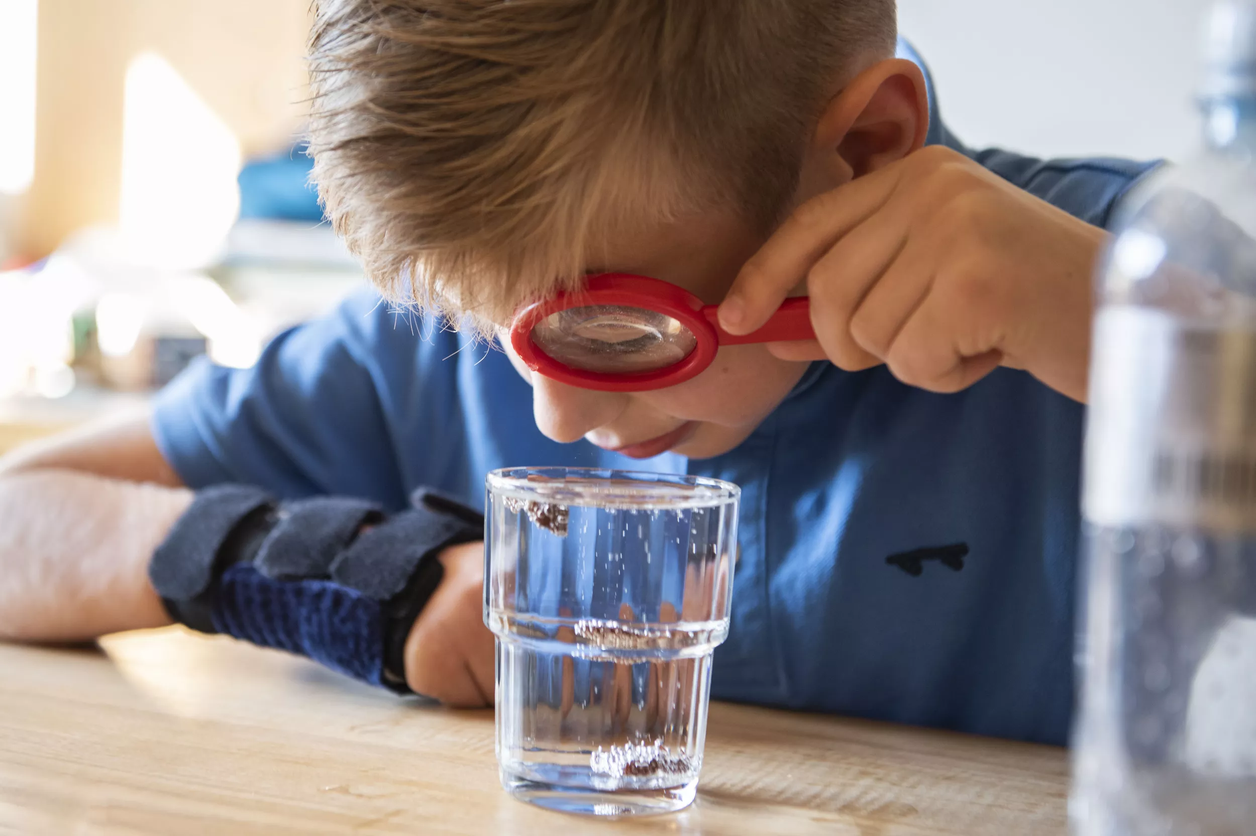 Ein junger Reha-Patient hält eine Lupe in der linken Hand und schaut in ein Glas Wasser