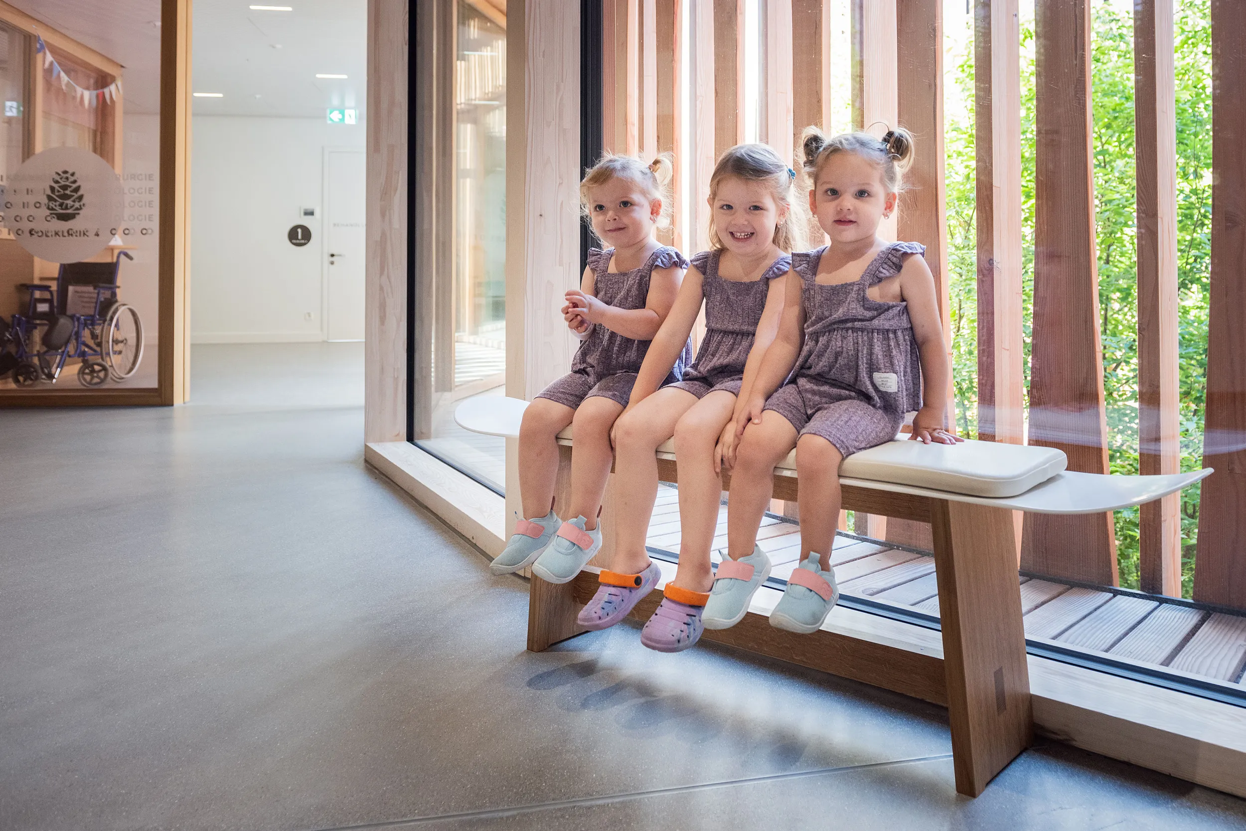 Drei kleine Mädchen sitzen auf einer Bank bestehend aus einem Snowboard im Kinderspital Zürich