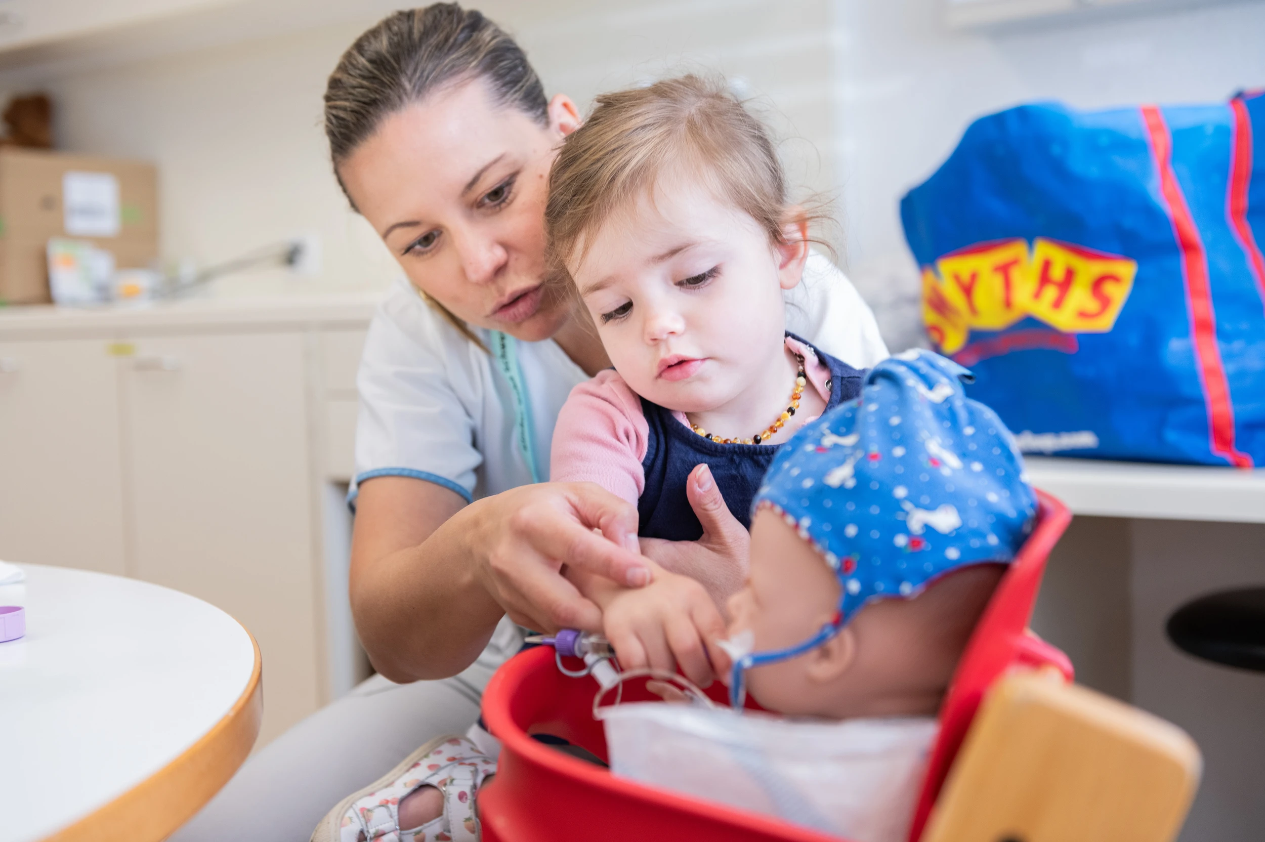 Eine Pflegefachfrau in der Kinder-Reha Schweiz erklärt einem Kind die Pflege an einer Puppe