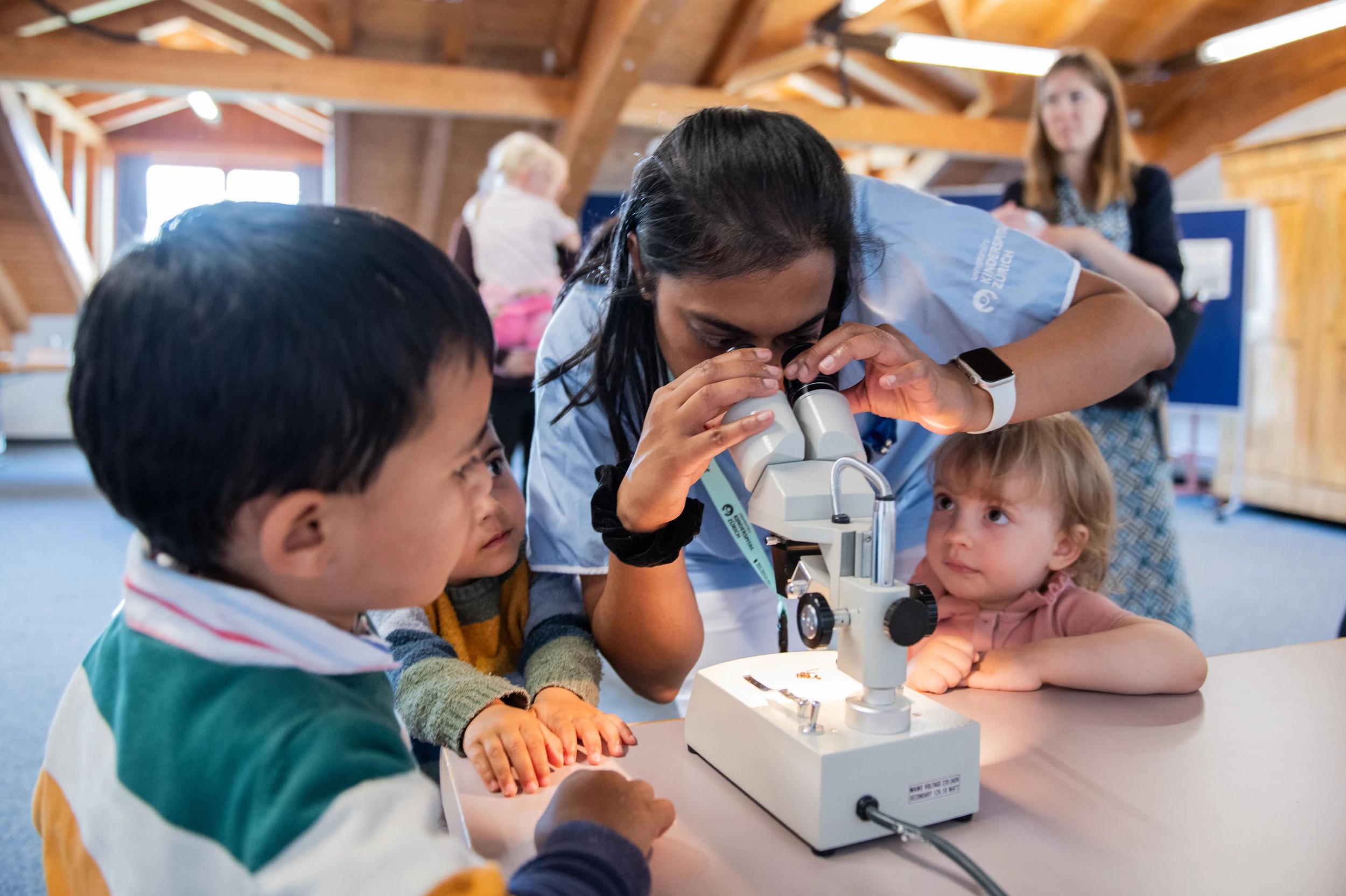Eine Pflegefachfrau und zwei Kinder untersuchen schauen durch ein Mikroskop am Tag der offenen Tür in der Kinder-Reha Schweiz