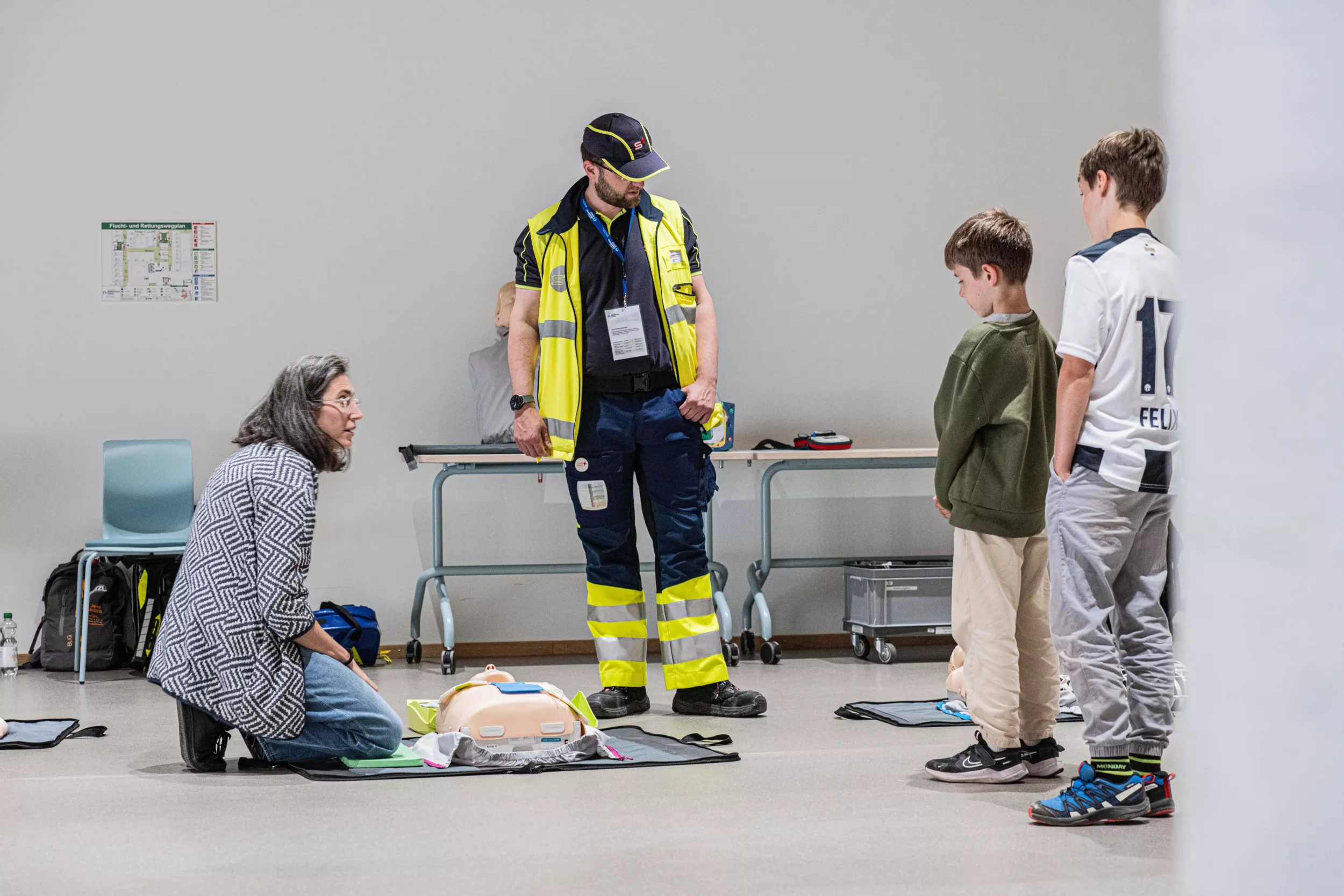 Samariter erklärt interessierten Kindern die Erste-Hilfe an einer Puppe