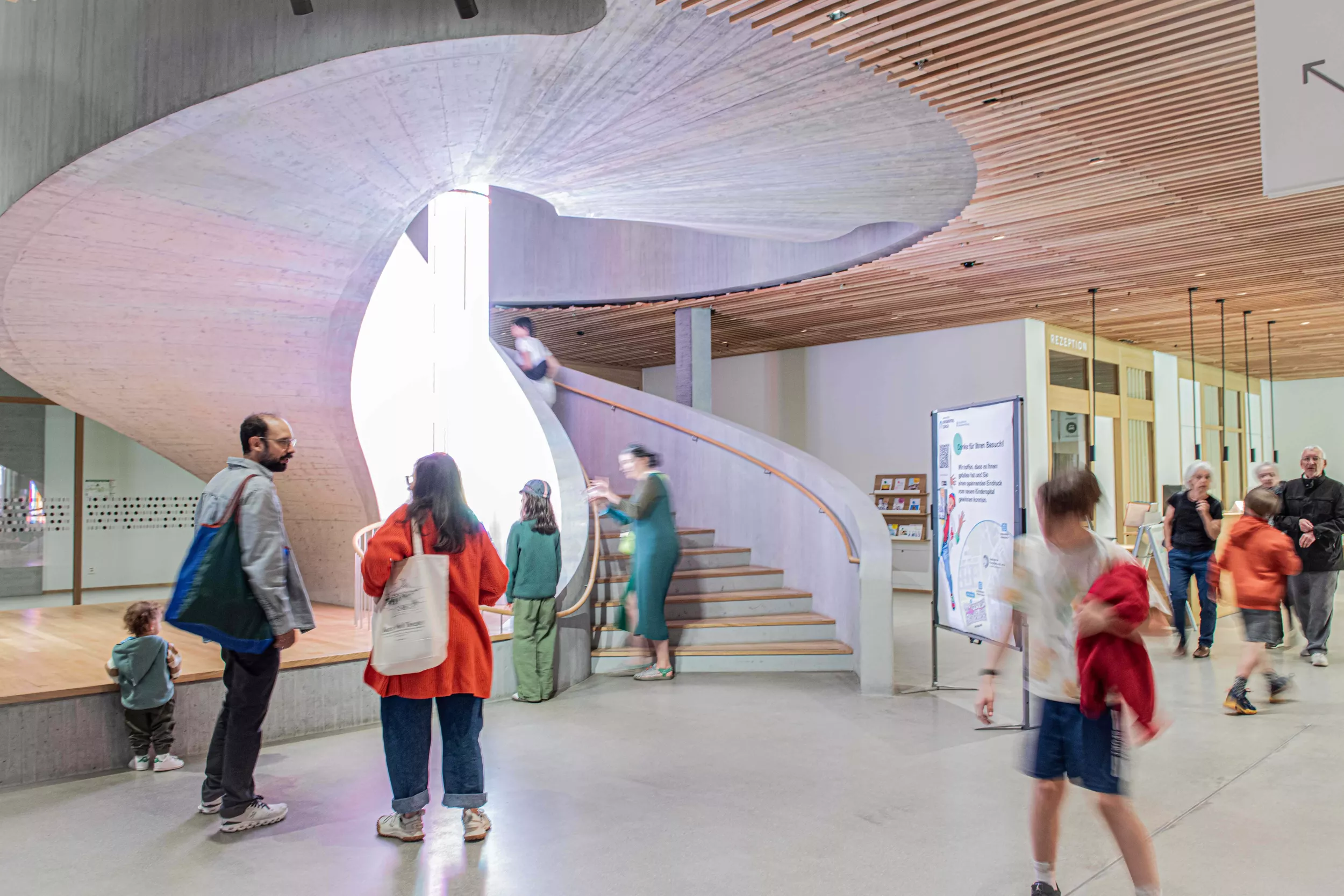 Besuchende im Foyer mit markanter Rundtreppe im Hintergrund