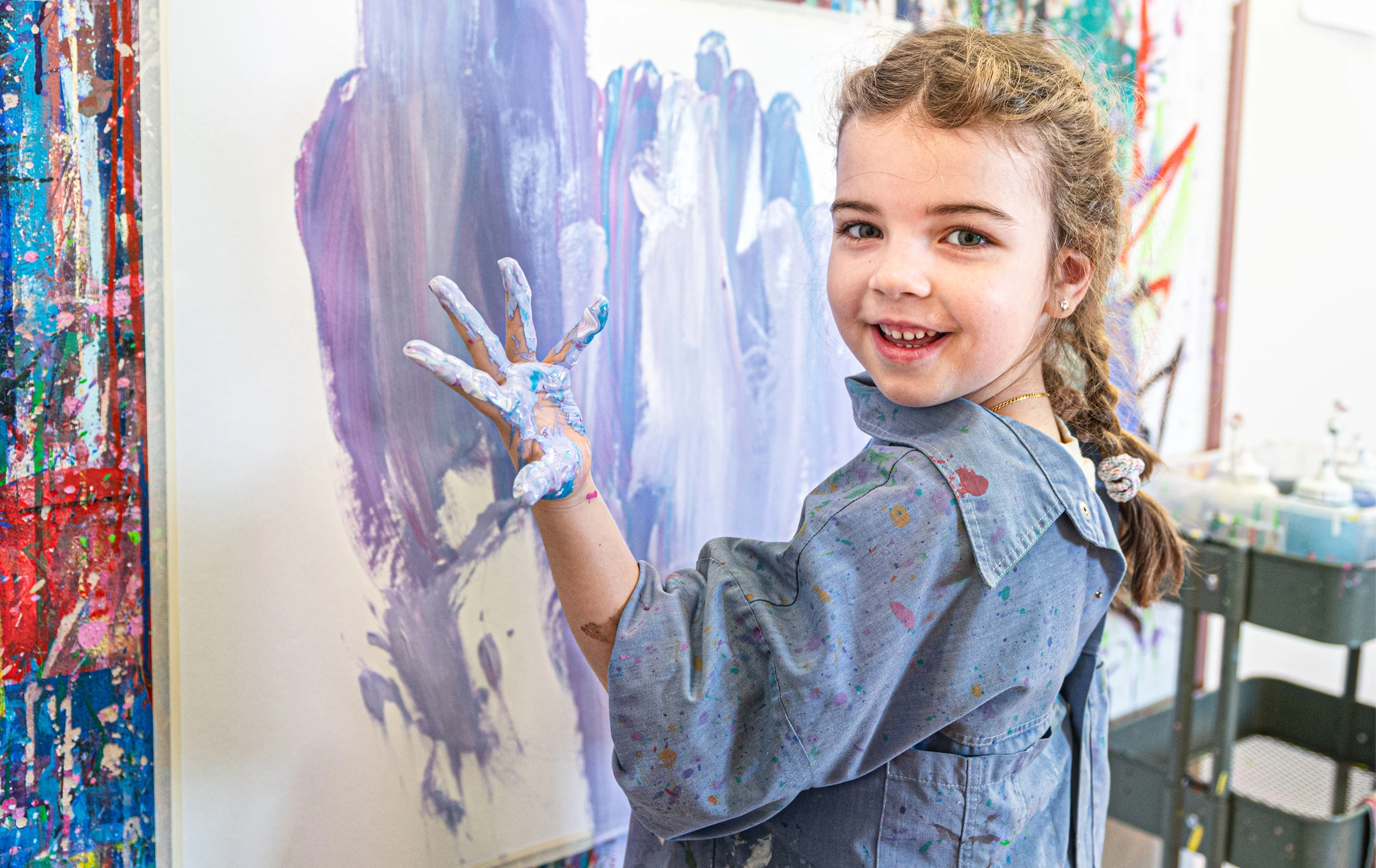 Patientin Vivian in der Kinder-Reha Schweiz malt mit ihren Händen auf einer Leinwand.