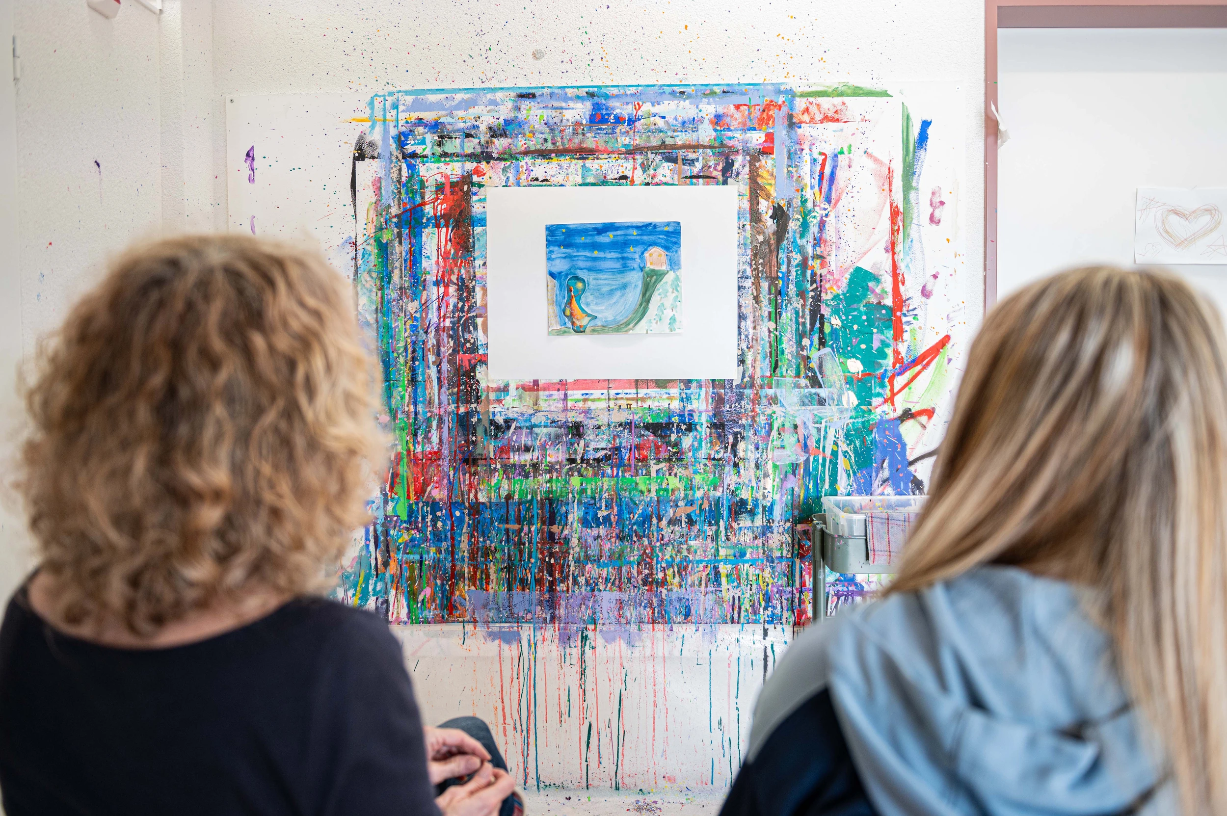 Patientin Joelle in der Kinder-Reha Schweiz betrachtet zusammen mit einer Kunsttherapeutin ihr gemaltes Bild.